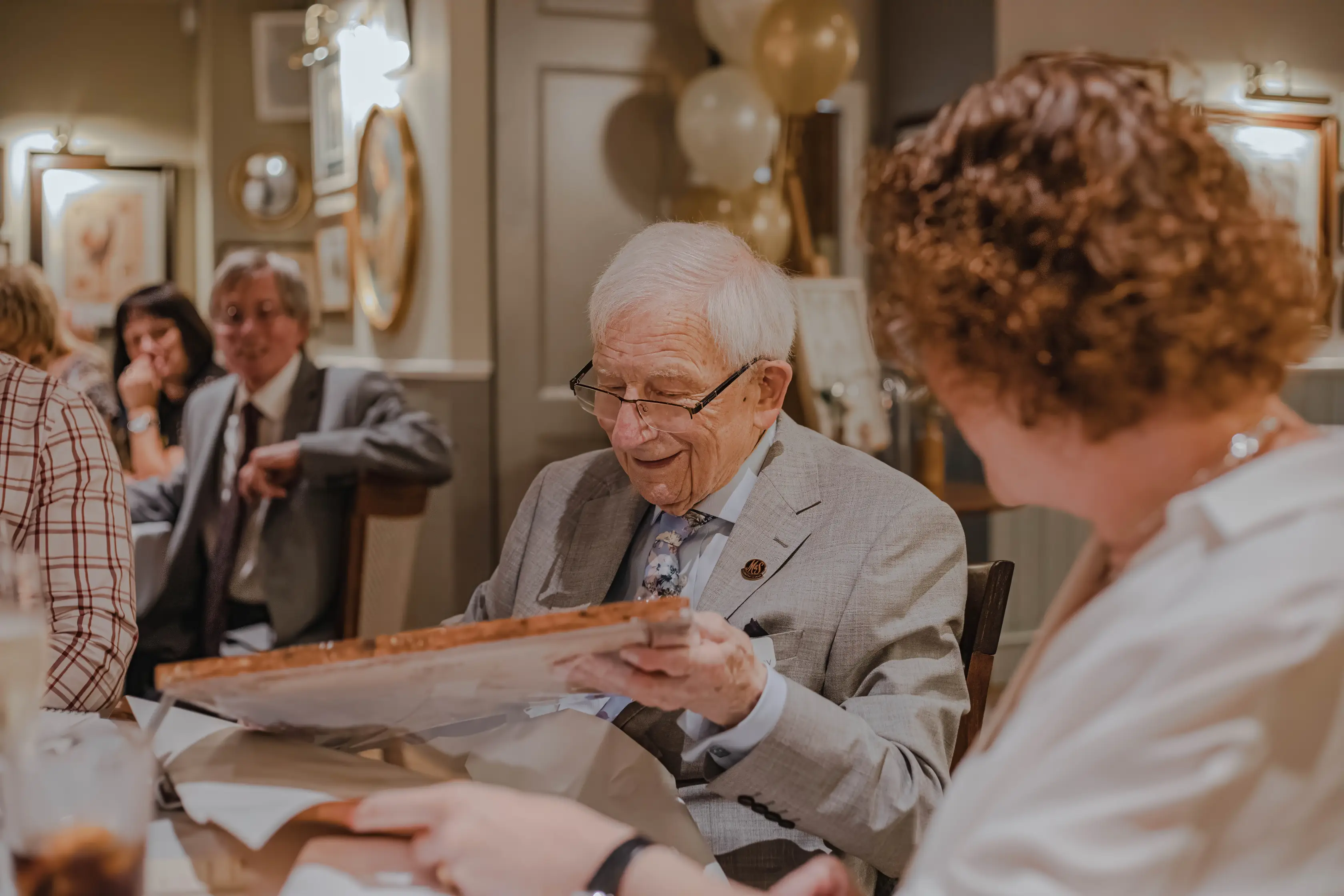 A group of well dressed elderly folks and their families, at an event, enjoying themselves.